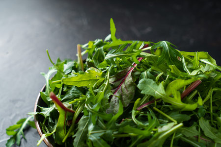 Mix salad greens. Arugula, lettuce, spinach in black bowl on stone countertopの写真素材