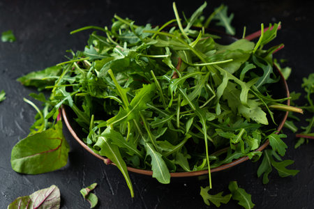 Mix salad greens. Arugula, lettuce, spinach in black bowl on stone countertop