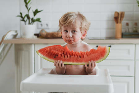 Adorable little boy eating juicy watermelon while sitting at the childrens tableの写真素材