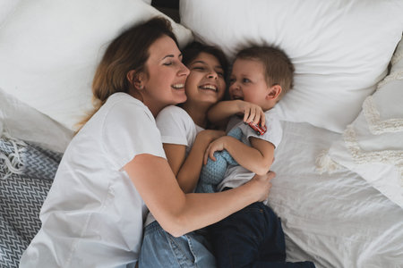charming mother and her children, daughter and little son have fun at home on the bed