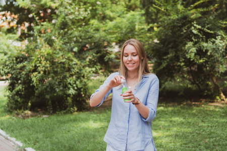 young charming woman blowing bubbles in the park and having fun