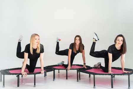Three adorable fitness women In sportswear jumping on sport trampoline White backgroundの写真素材