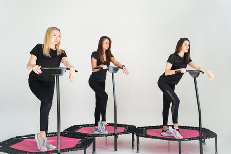 Three adorable fitness women In sportswear jumping on sport trampoline White backgroundの写真素材
