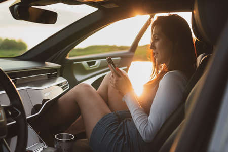 beautiful young woman travel on the roads by car, parked on the side of the road and uses a smartphone.の写真素材