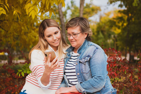 charming women in casual style, mom and daughter are sitting on a bench in a beautiful autumn park...