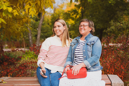 charming women in casual style, mom and daughter are sitting on a bench in a beautiful autumn park...