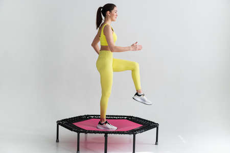 young fitness woman In sportswear jumping on sport trampoline White backgroundの写真素材