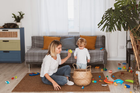 Pretty young woman, housewife messaging on smartphone while sitting on the couch with her little son at home in the living roomの写真素材