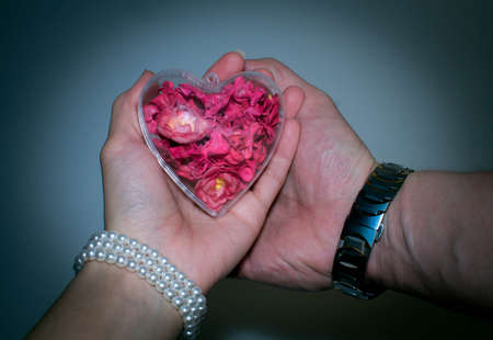 glass heart with red flowers inside women's and men's handの写真素材