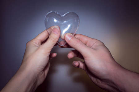 male and female hand holding a transparent glass heartの写真素材