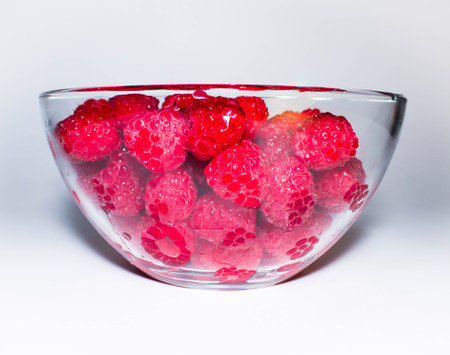 Fresh juicy red raspberry in a transparent glass bowl