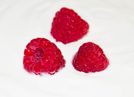Three juicy raspberries on white yogurt close upの写真素材