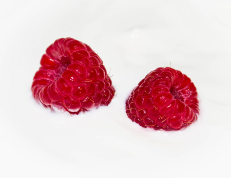 Two juicy raspberries on white yogurt close upの写真素材