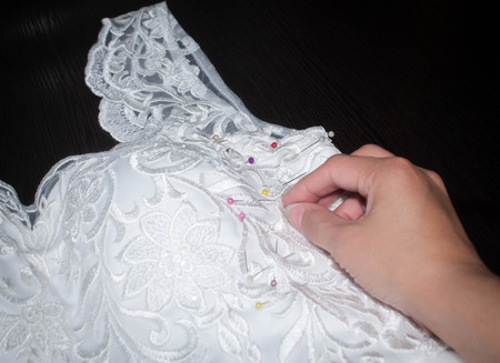 Sewing the wedding dress, a hand seamstress holding a needle over the fabric patternの写真素材