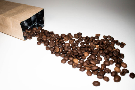 coffee beans are poured from a Kraft paper bag, isolated on a white backgroundの写真素材