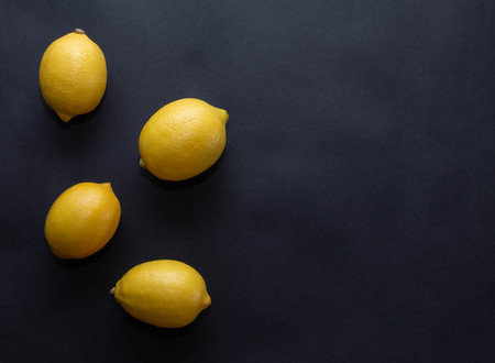 four yellow lemons on a dark black backgroundの写真素材