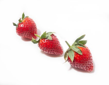 three strawberry berries lie in a diagonal line isolated on a white backgroundの写真素材