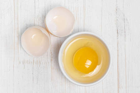 Row fresh egg in ceramic small white plate and two parts of shell above view on painted wooden background macroの写真素材