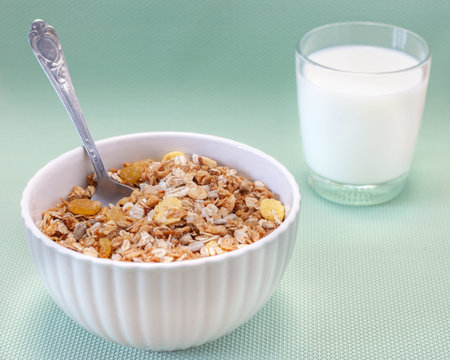 Homemade cooked oatmeal cereals with ceramic mug, metal spoon and glass of milk on blue background