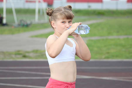 a sporty girl drinks water from a bottle and smiles sweetly at a running stadiumのeditorial素材