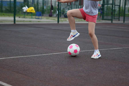 Young girl soccer player with a pink soccer ball isolated on a soccer field or brown backgroundのeditorial素材