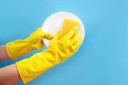 Hands in rubber gloves close wash the plate with a sponge and foam. Dishwashing detergent, clean. Blue background.の写真素材