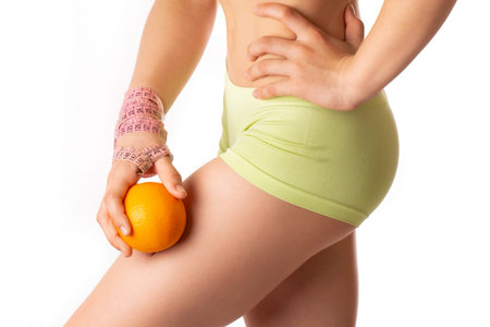 A young woman holds an orange citrus on a white background. The concept of cellulite problem