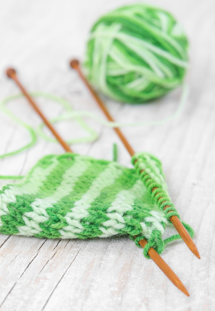 Knitting pattern of green yarn on wooden needles and skein on a wooden backgroundの写真素材