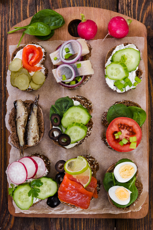Small sandwiches with vegetables, fish and sausage on board on wooden background. Top view.の写真素材