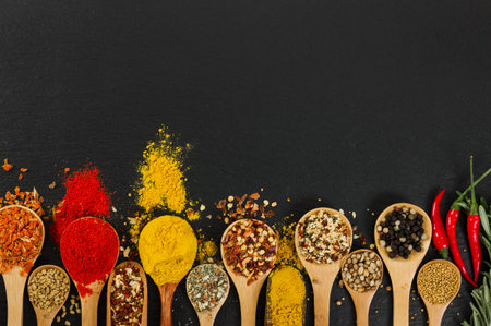 Various spices in wooden spoons on black slate background. Top view.の写真素材