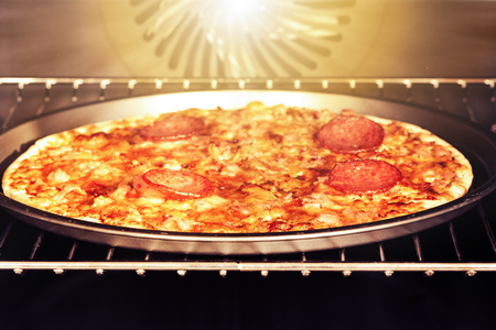 Homemade pizza with cheese and salami in an electric oven. Vintage toning.の写真素材