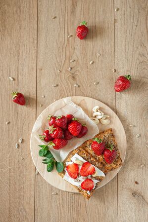 Light breakfast with strawberry berries and cream cheese. In the rustic style on a wooden background and a round wooden stand. Vertical photo.の写真素材
