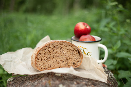 Ripe red apples in a mug. A hunk of bread. Snack in the woods.