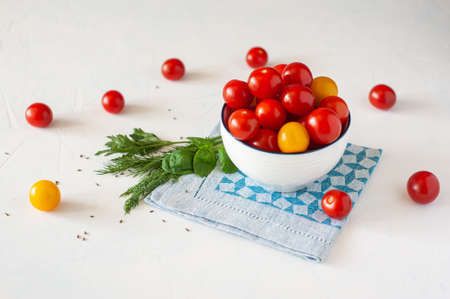 Cherry tomatoes of different colors in a white bowl on a glued blue napkin. On a light blue background under the concrete.の写真素材