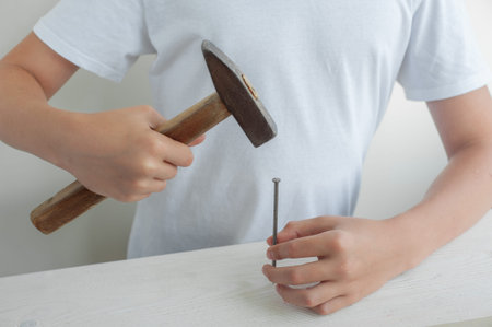The teenagers hands with a hammer and a nail. The boy learns to hammer nails. White background.
