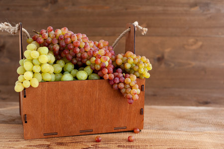 Harvest grapes. Ripe bunches of grapes in a wooden basket on a wooden background. Horizontal photo....