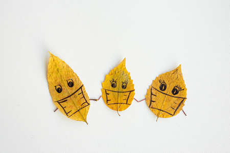 Covid concept. Yellow autumn leaves with drawings of faces in medical masks. The image of the family during the coronavirus epidemic.の写真素材
