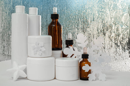 A set of winter care cosmetics against the background of the frosty window. White jars, bottles and...