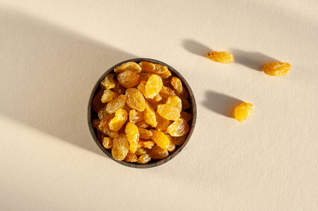 Raisins of yellow grapes in a wooden plate on a beige background in bright sunlight. Healthy sweets....
