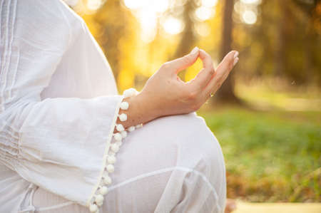 A girl plus a size in a white suit with a hood doing yoga and meditating in the park. Yoga and wellness concept Hands close upの写真素材