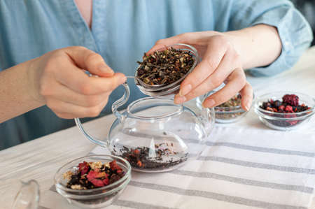 several varieties of herbal and berry tea and a kettle with hot fresh tea on a wooden tray and beige linen tablecloth. Vertical photo.の写真素材