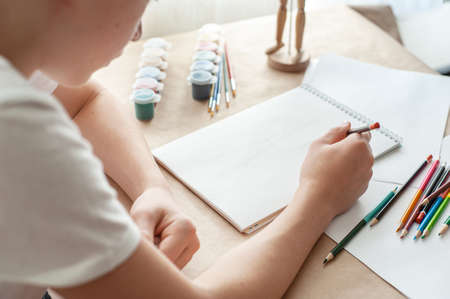 A teenage child draws. The hand of a teenage boy with a pencil. Creative hobby. Drawing lesson. Close-up and selective focus.の写真素材