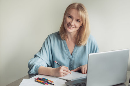 Hobbies and online training. A beautiful blonde woman draws in an album on an online lesson. A woman...