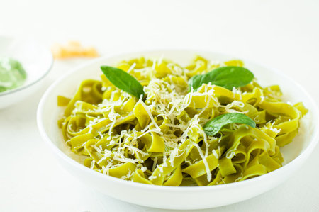 Green noodles with spinach and parmesan cheese in a white plate on a white table. Basic ingredients....