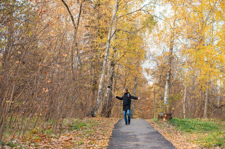 A teenage boy walks through an autumn park and shoots a video. A Caucasian boy in a black jacket...