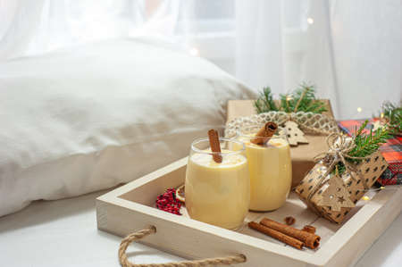 Two glasses of eggnog on a tray of Christmas presents in bed. Christmas breakfast. Sweet winter egg dessert. Selective focusの写真素材