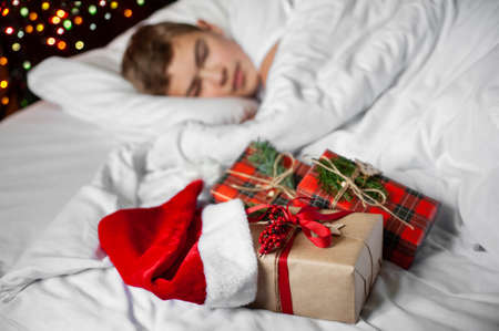 A teenage boy sleeps in bed , with Christmas presents lying nearby. The room is decorated with Christmas decoration. Christmas morning.の写真素材