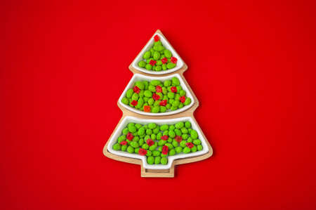 Christmas sweets. Candy in a plate in the shape of a Christmas tree on a red background. Place for your text. View from above. Candy bar. Banner.の写真素材