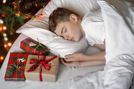 A teenage boy sleeps in bed , with Christmas presents lying nearby. The room is decorated with Christmas decoration. Christmas morning.の写真素材