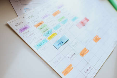 Close-up of the school schedule for the week out of focus with selective focus. The schedule is painted with colorful markers on a white desktop.の写真素材